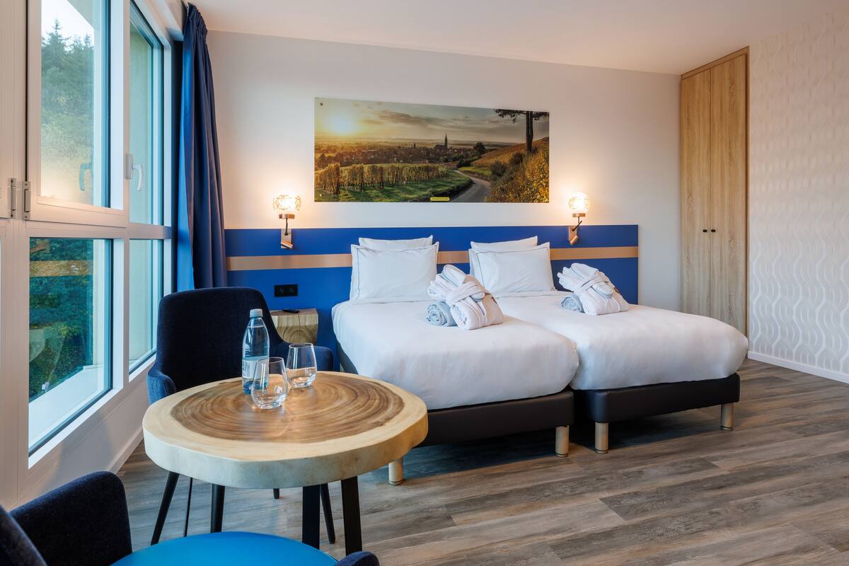 Habitación de hotel con una cama, una mesa redonda de madera, una silla y un ventanal grande.