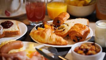 Ein Frühstückstisch mit Croissants, Toast, Würstchen und einer Obstschale.