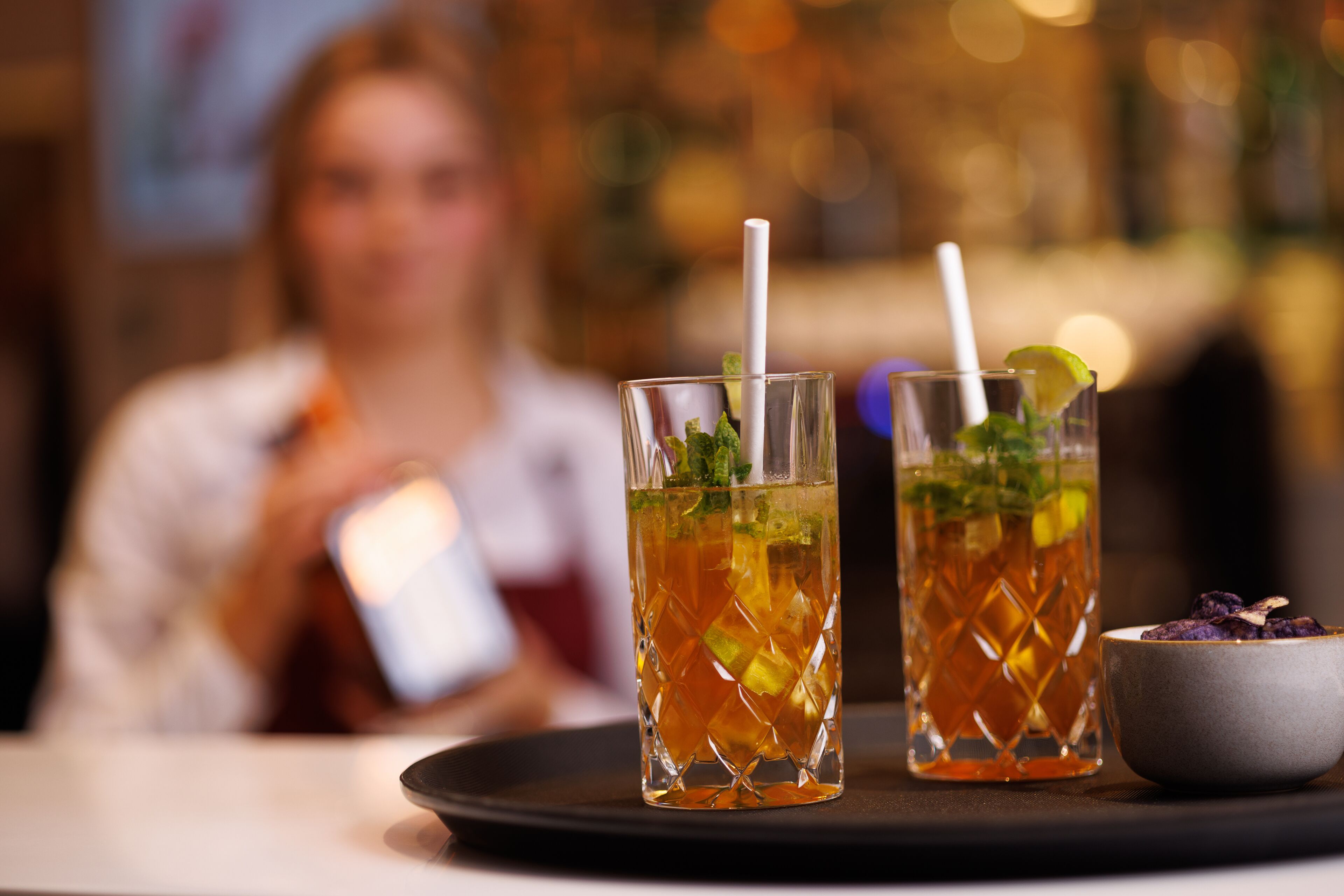 Two glasses of iced tea with straws and mint leaves on a tray.