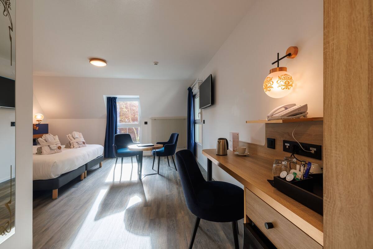 Una habitación de hotel moderna con cama, escritorio, silla, televisor y ventana con cortinas.