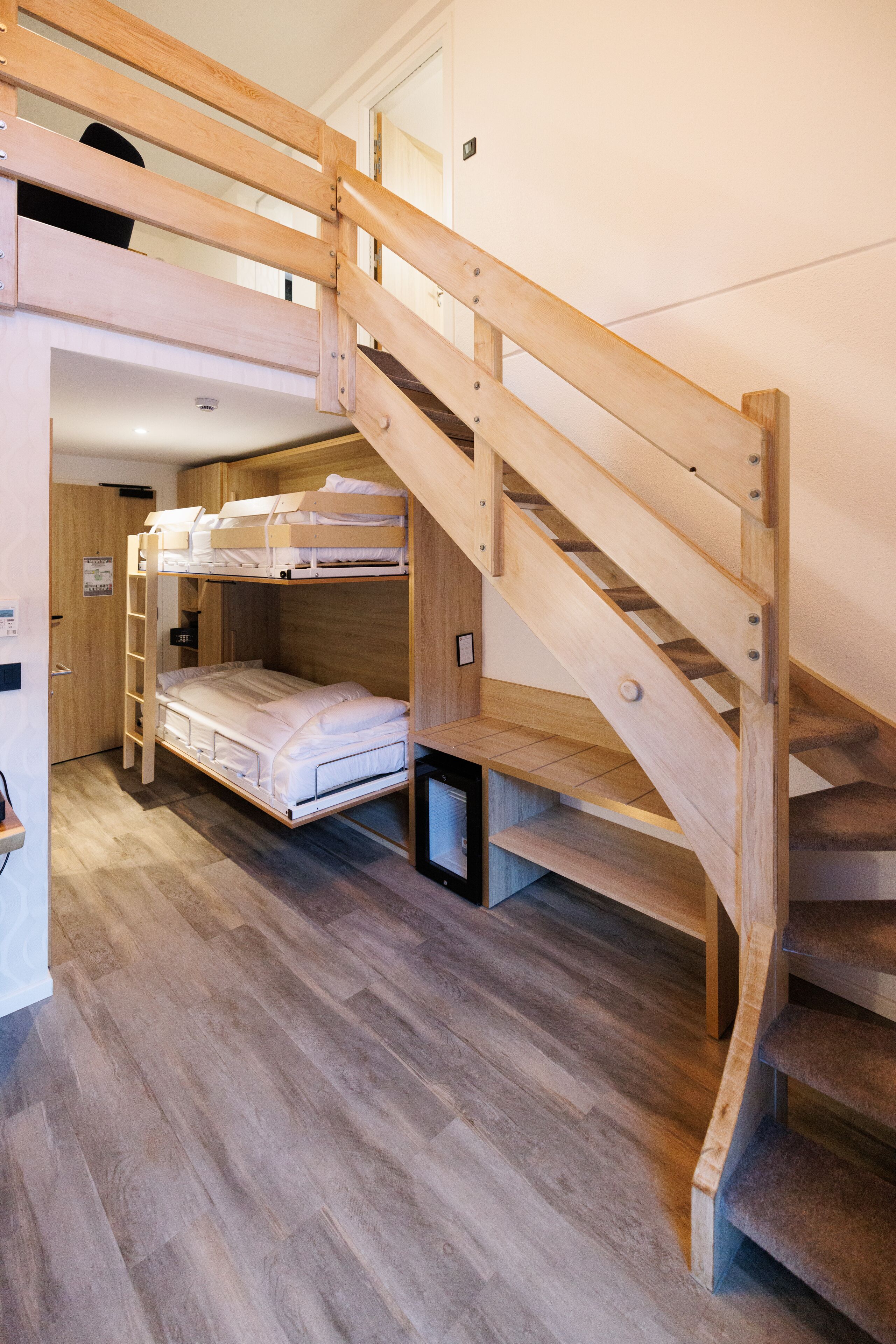 A bunk bed with a wooden ladder, a desk, and a small shelf.