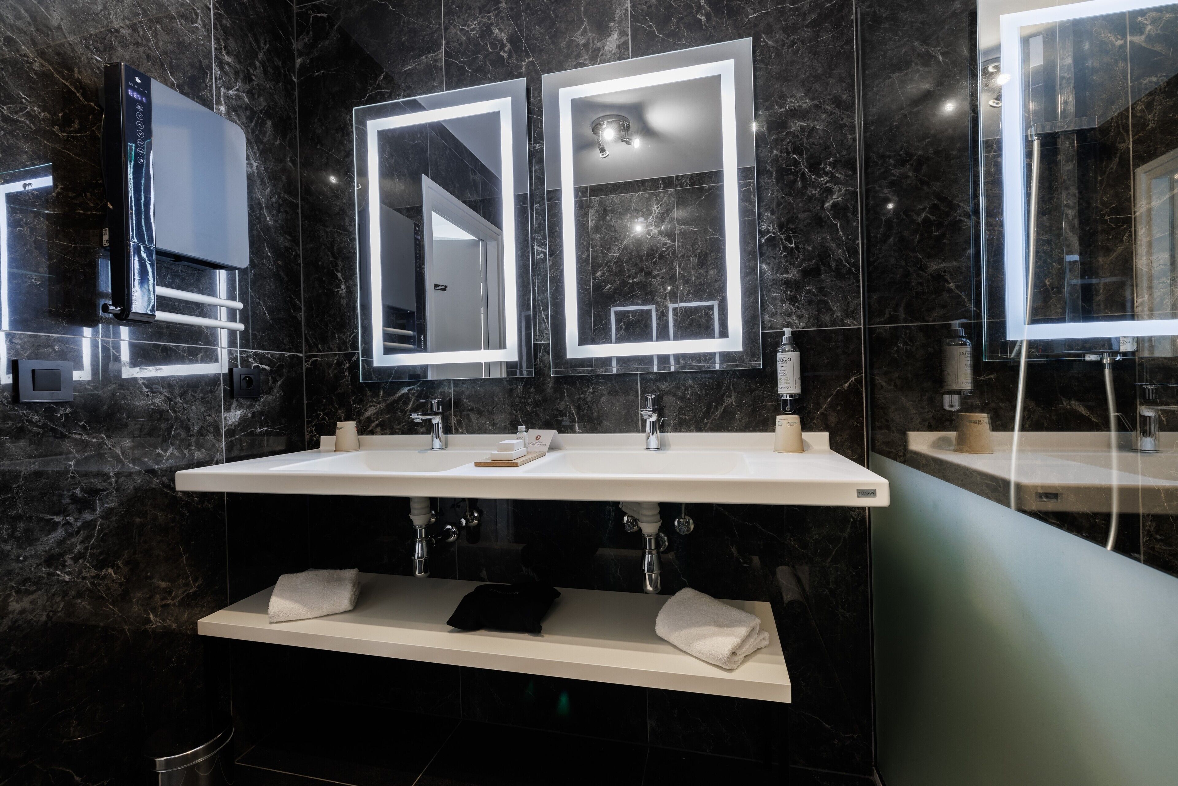 Ein modernes Badezimmer mit einem Doppelwaschbecken, Marmorwänden und einem integrierten Spiegel.