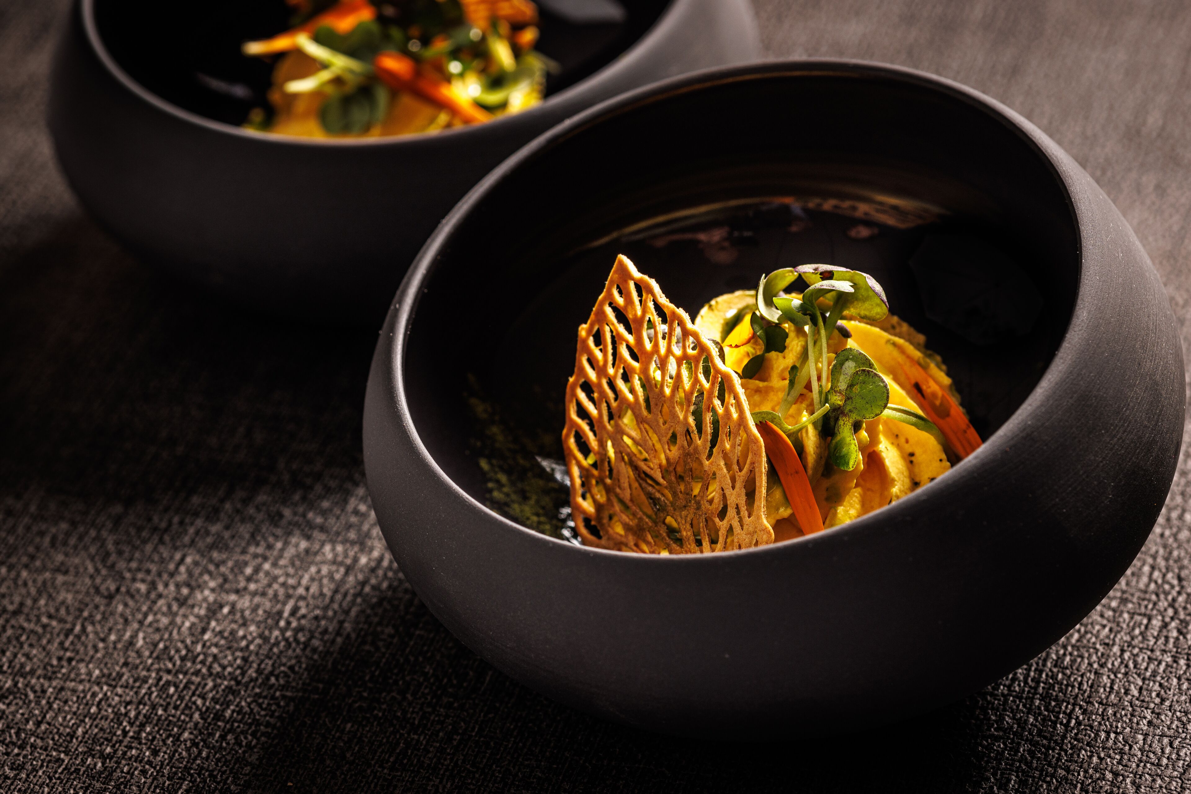 Two black bowls with a dish inside, placed on a textured surface.