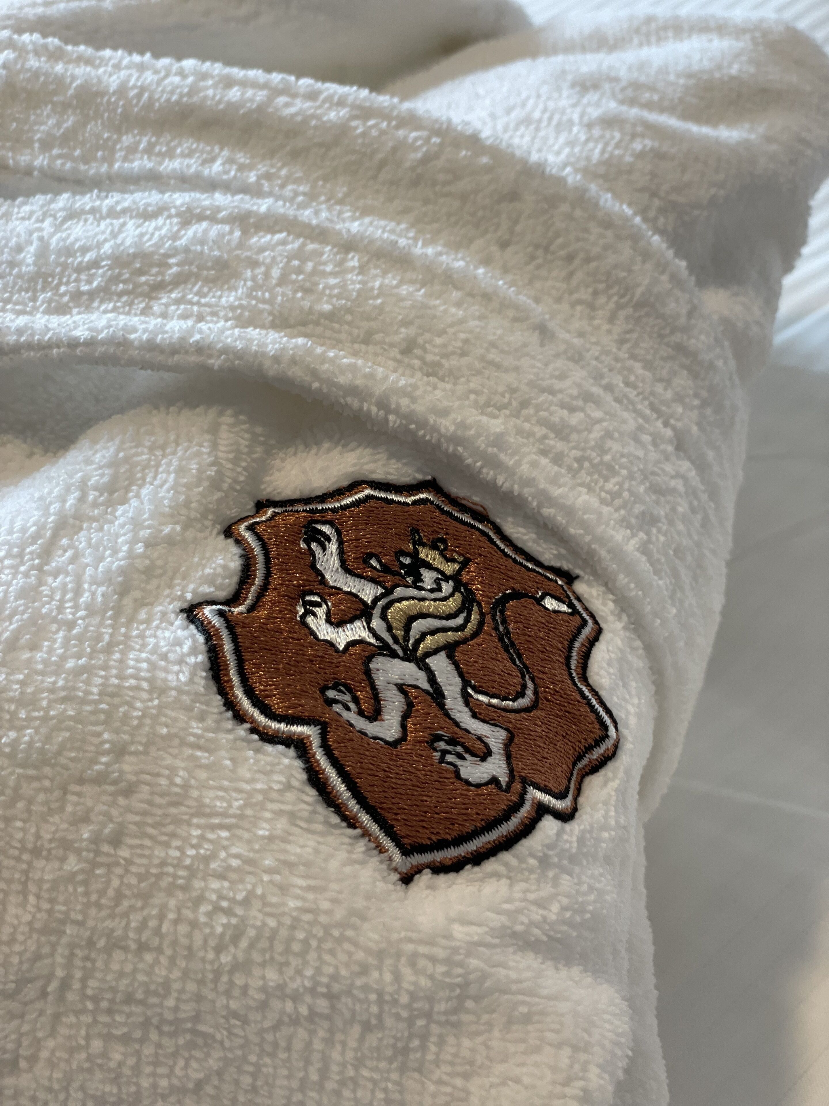 A white textured fabric with a brown embroidered emblem featuring a lion.