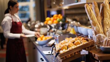Disposição de buffet com diversos alimentos, incluindo pão, doces e frutas.