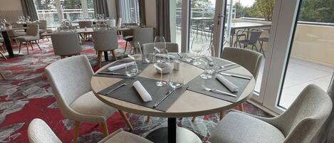 A dining area with round tables, grey upholstered chairs, and a red patterned carpet.