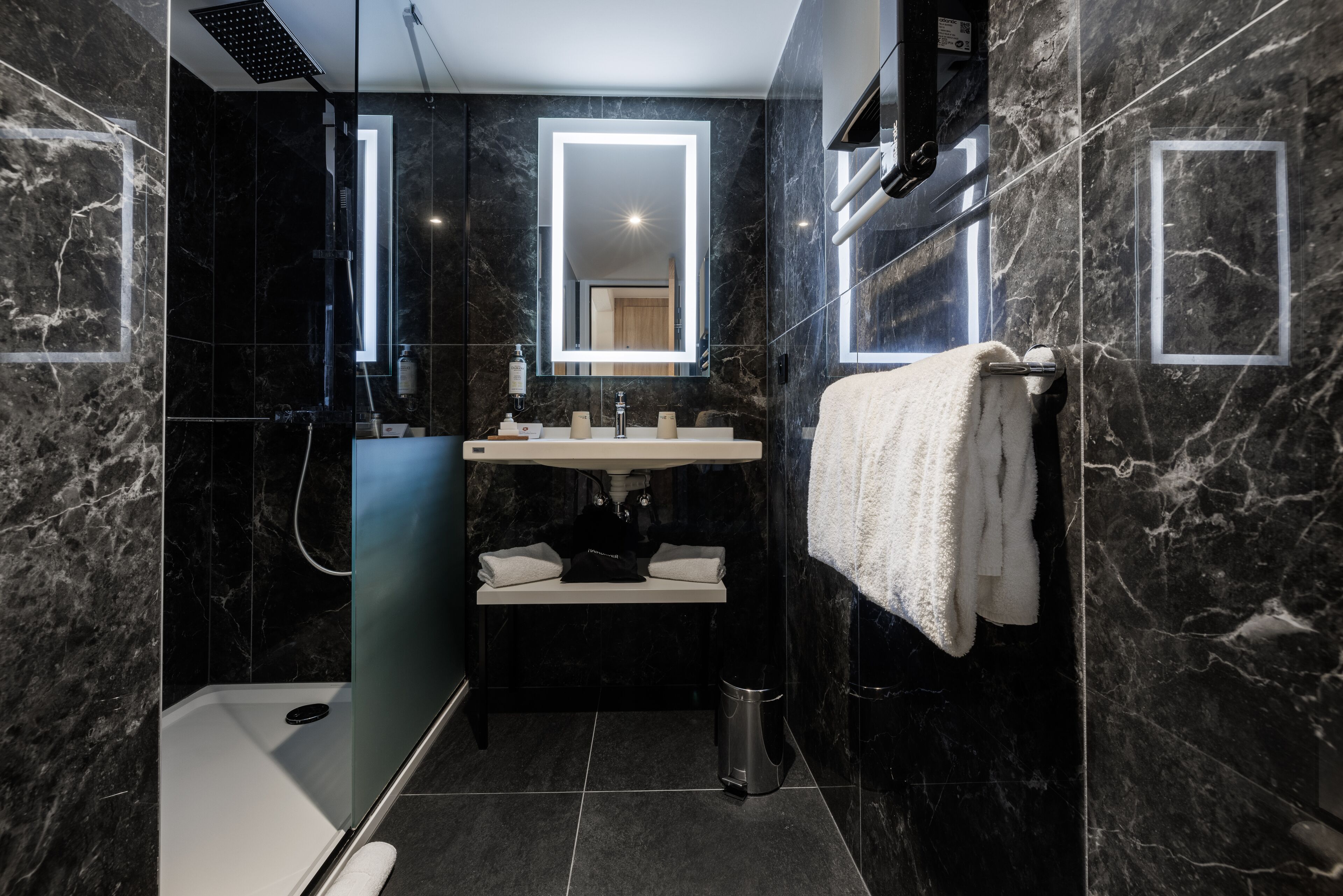 Un baño moderno con ducha envuelta en vidrio, tocador con espejo y perchero.