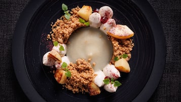 A dessert on a black plate with crumbled topping, fruit, and mint leaves.