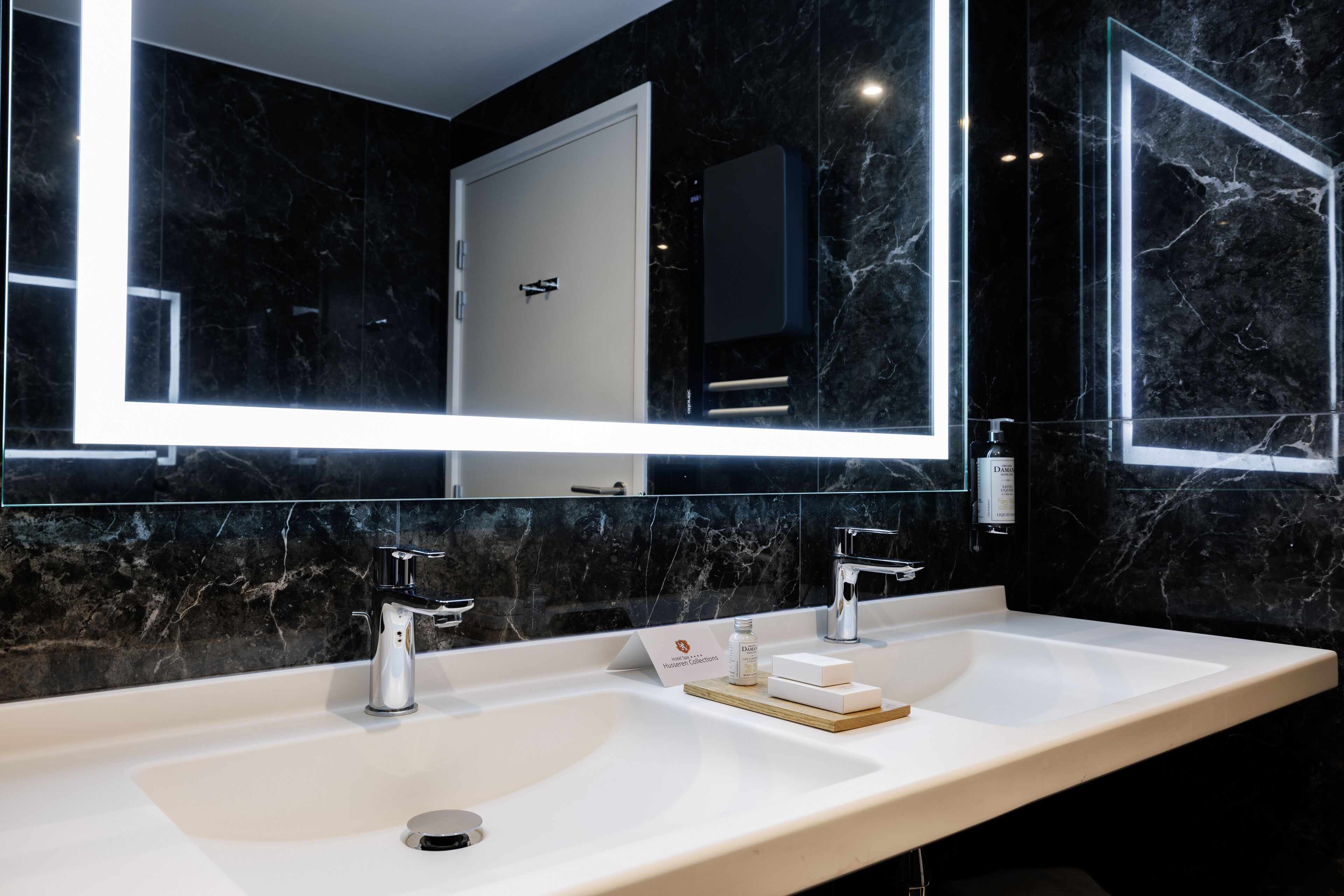 A modern bathroom with a large mirror, two sinks, and a marble backsplash.