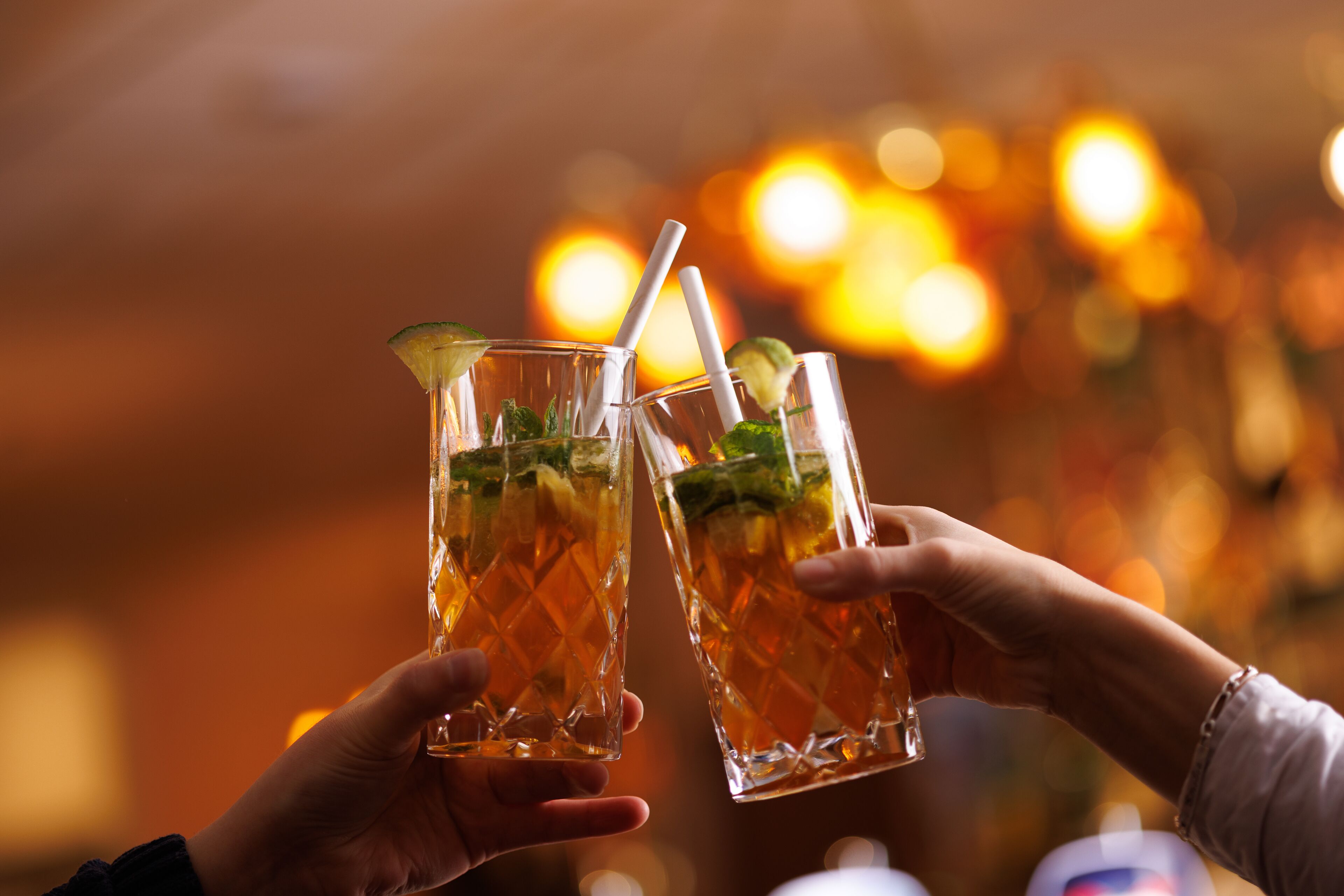 Due mani che sorreggono bicchieri con una bevanda, probabilmente in un bar.