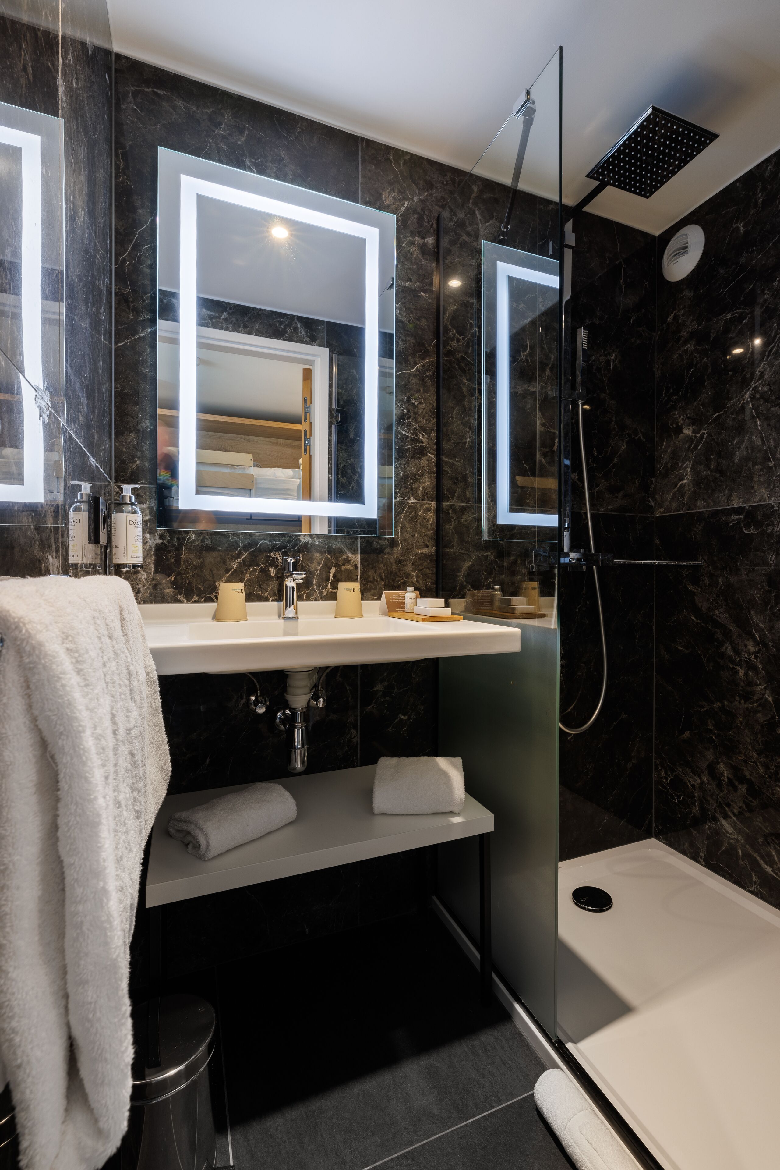 Une salle de bain moderne avec un double vasque, une douche à parois de verre et des murs en marbre.
