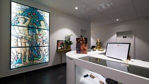 Un área de recepción con un ventanal de vitral, un mostrador de recepción, una planta en maceta y un cartel.