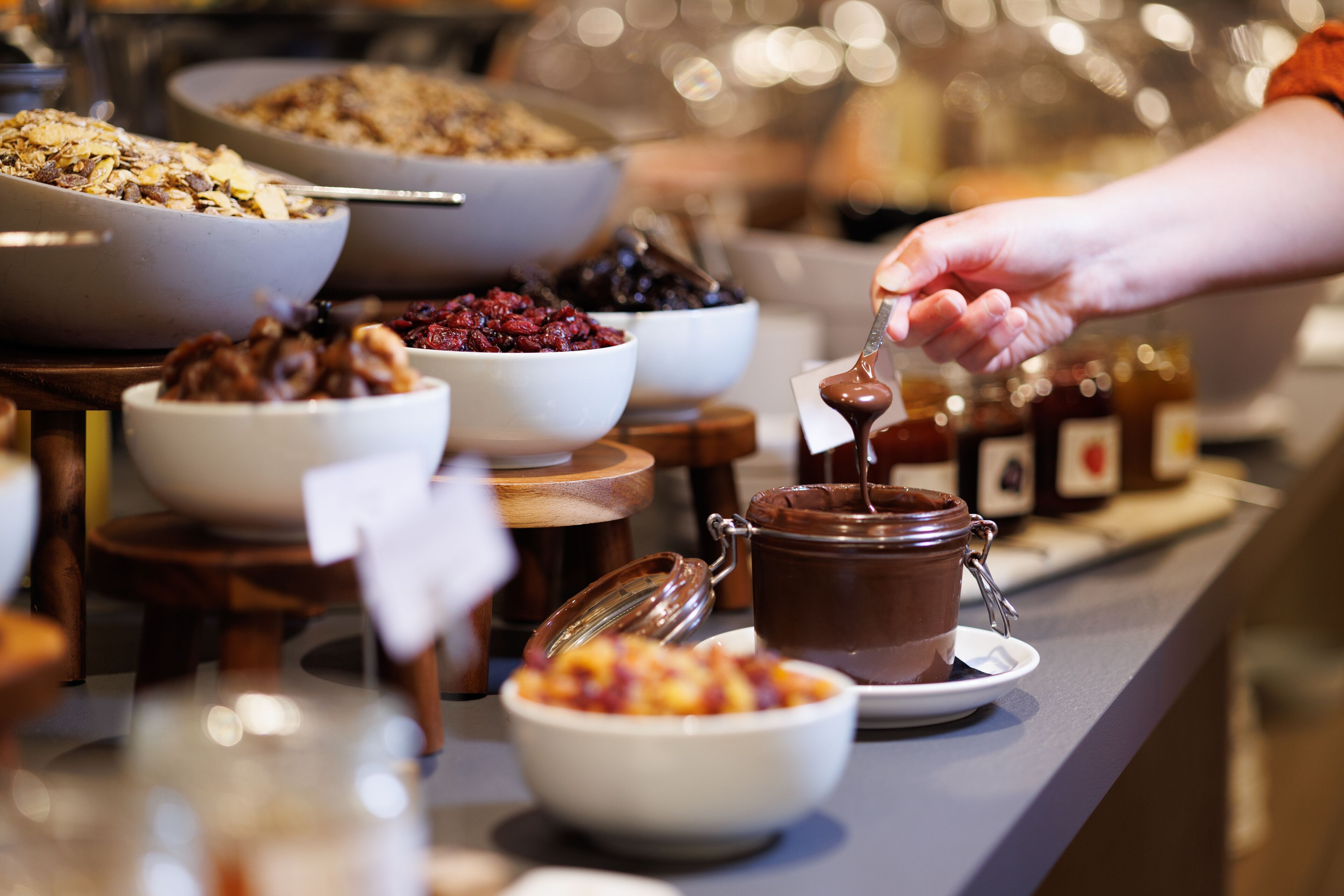 A buffet with various food items including bowls of cereal, fruit, and a chocolate spread.