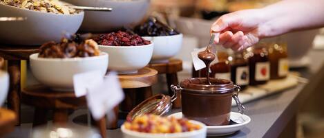 A buffet with various food items including bowls of cereal, fruit, and a chocolate spread.