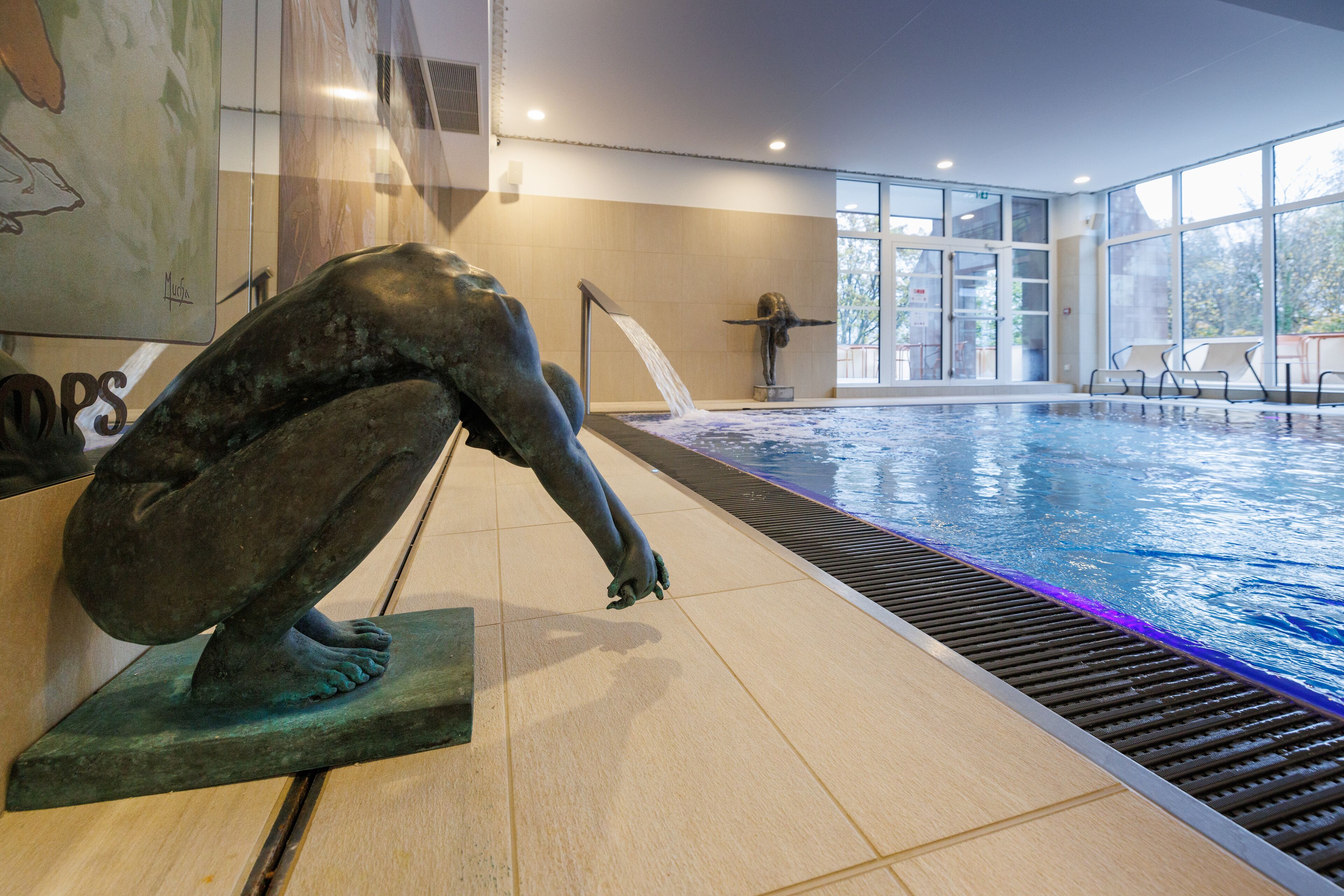 Una piscina con una escultura de una figura que se extiende hacia el agua, asientos interiores y ventanas amplias.
