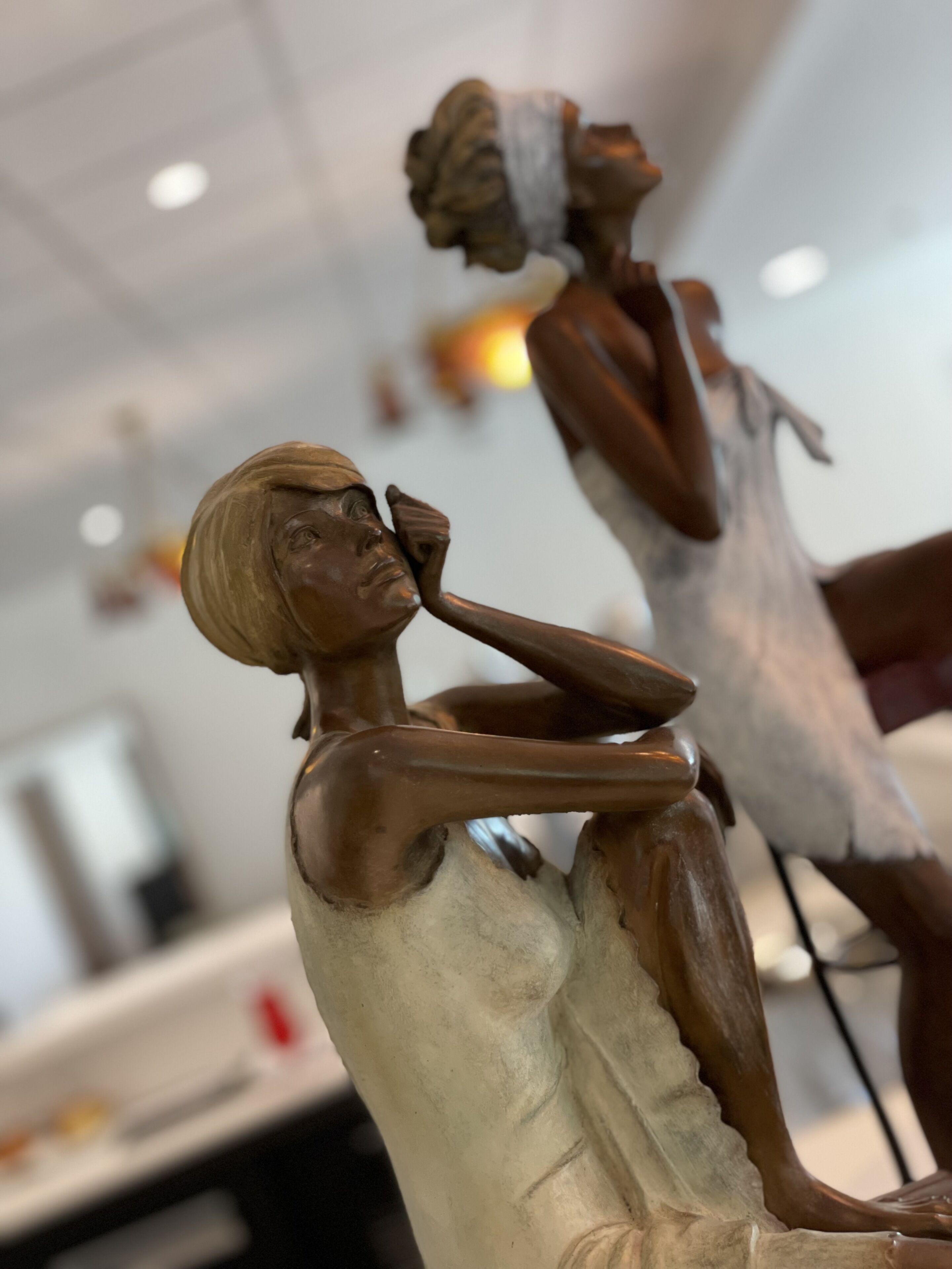 Une sculpture représentant une femme assise, dans une pose contemplative, et placée à l’intérieur.