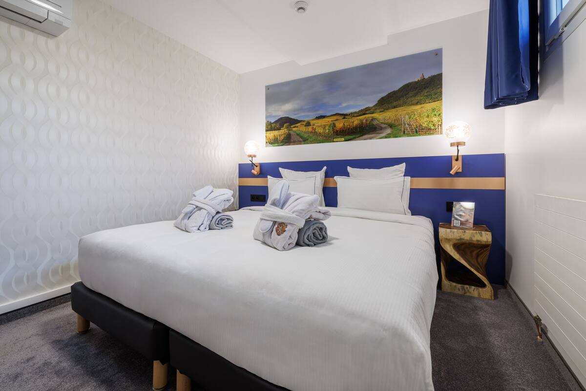 Una cama bien hecha con toallas, un cuadro en la pared y una mesita de noche con una lámpara.