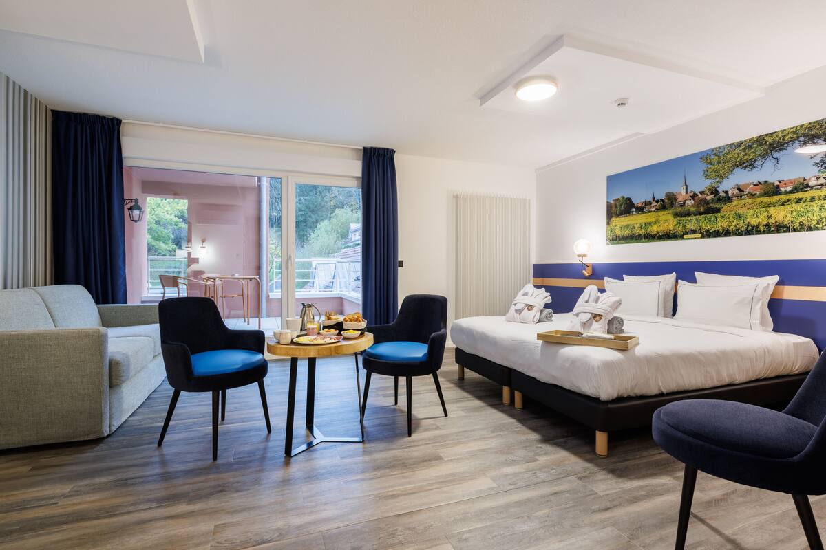 Una habitación de hotel con una cama, dos sillones, una mesita y un sofá.