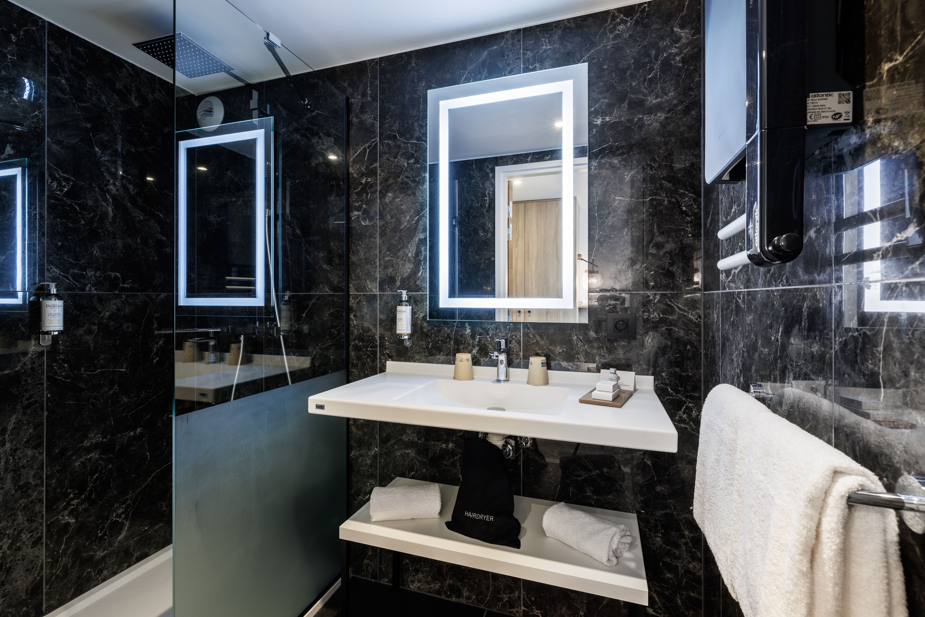 A modern bathroom with a black marble wall, a white sink, and a glass-enclosed shower area.