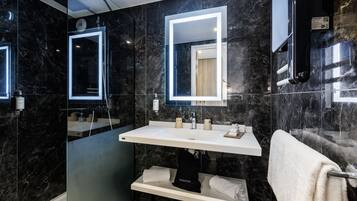 A modern bathroom with a black marble wall, a white sink, and a glass-enclosed shower area.