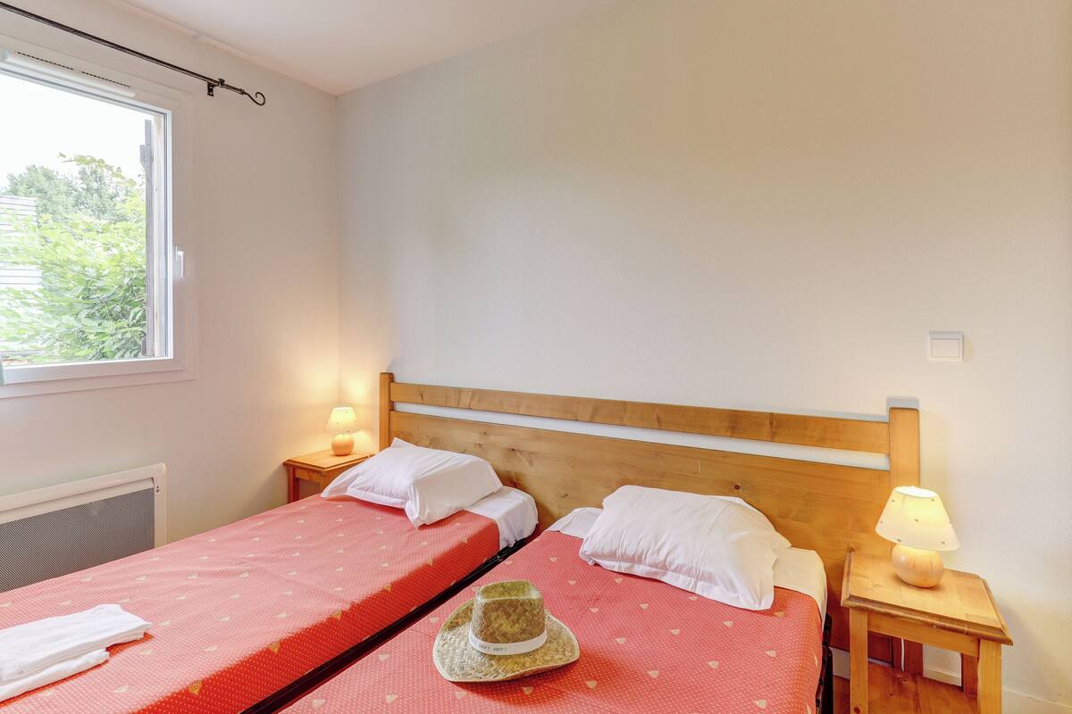 A bedroom with two beds, a window, and a nightstand with a lamp.