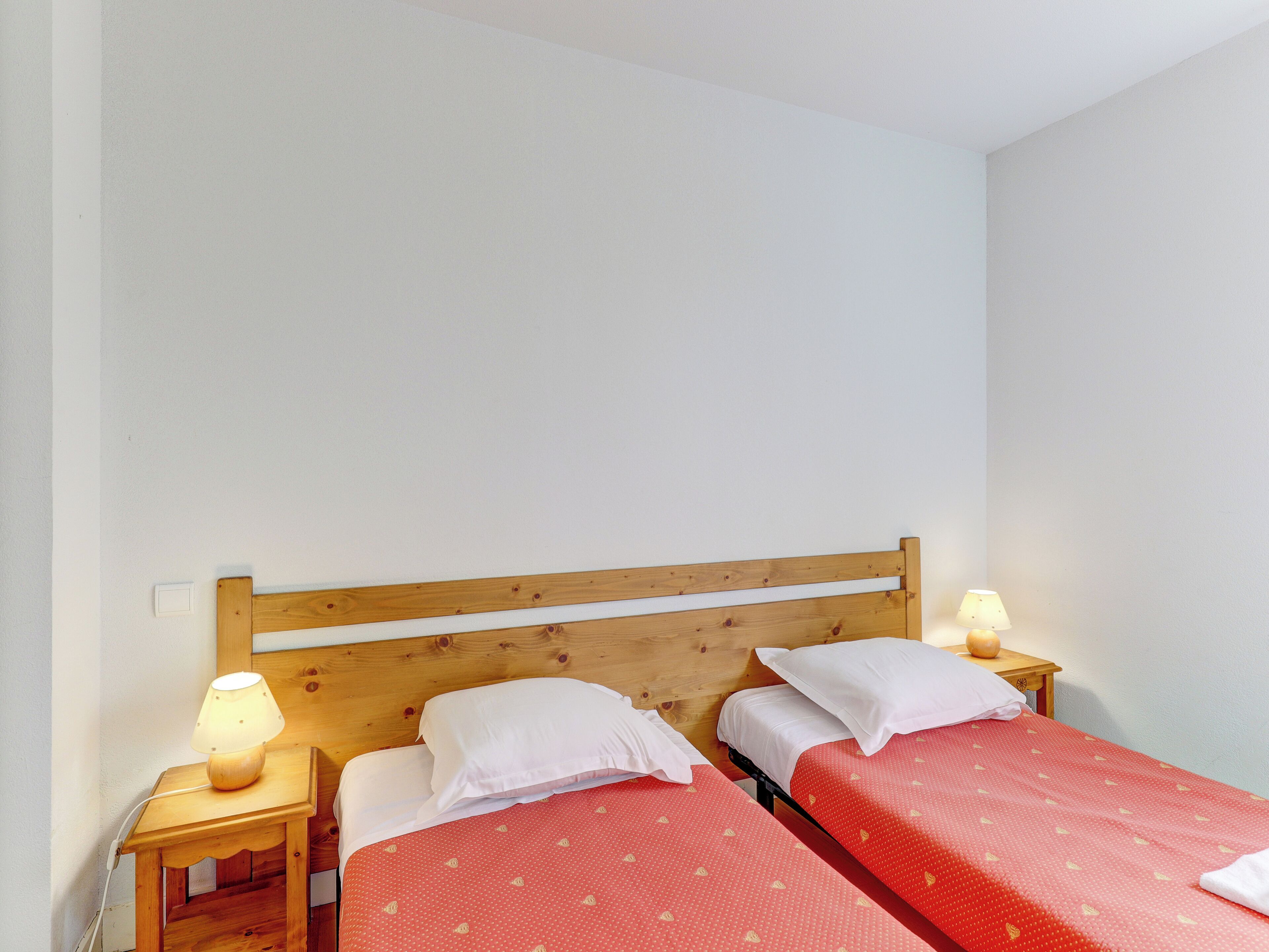 Une petite chambre propre, avec deux lits simples, des têtes de lit en bois et des lampes de chevet.