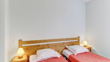 Une petite chambre propre, avec deux lits simples, des têtes de lit en bois et des lampes de chevet.