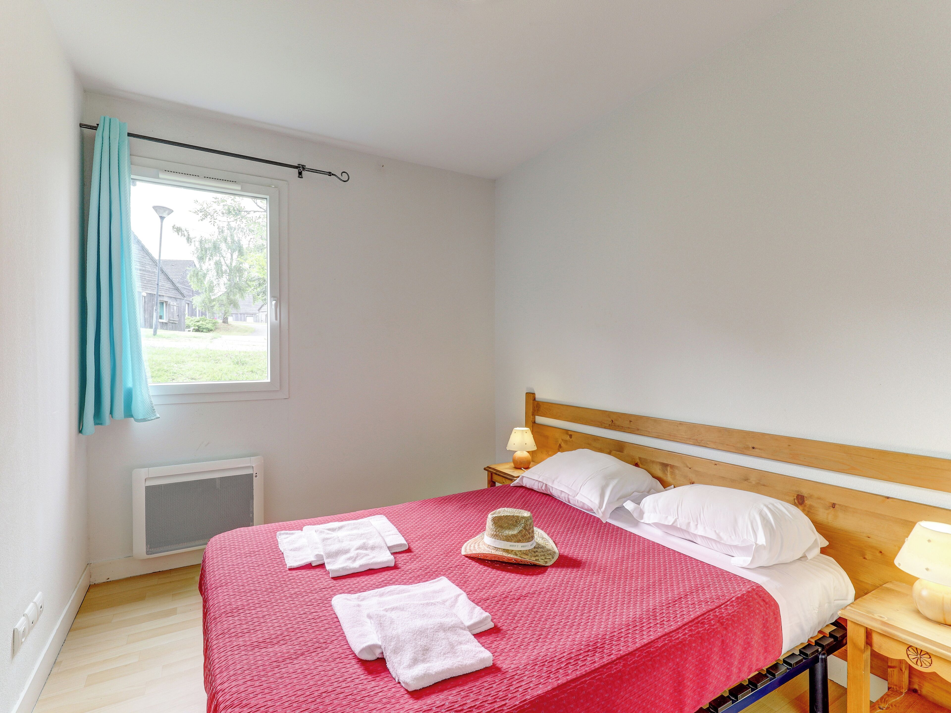 Un dormitorio con cama de madera, almohadas blancas, una manta roja y un sombrero sobre la cama.