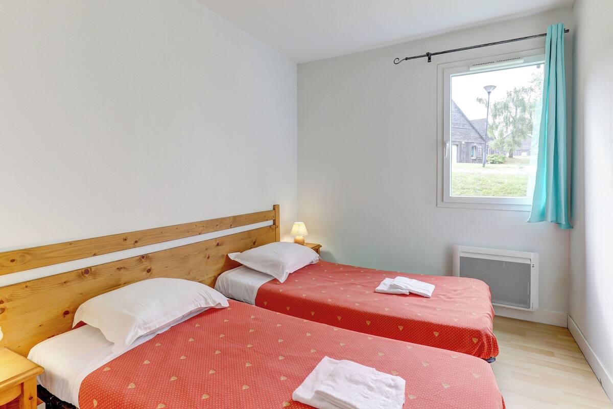 A room with two beds, a window with curtains, a radiator, and a lamp.