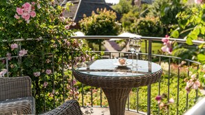 Une table en osier surmontée d’un plateau en verre, placée sur un balcon et entourée d’une rambarde en métal.