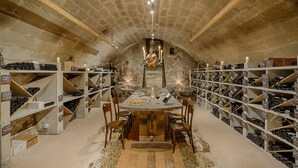 Une cave à vin avec des tables et des chaises en bois, entourée d’étagères remplies de bouteilles de vin.
