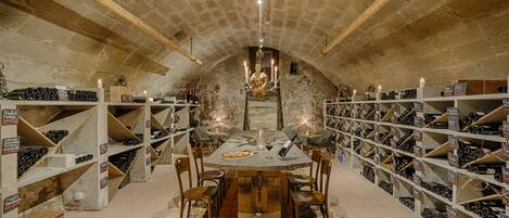 Una bodega con mesas y sillas de madera, rodeada de estanterías llenas de botellas de vino.