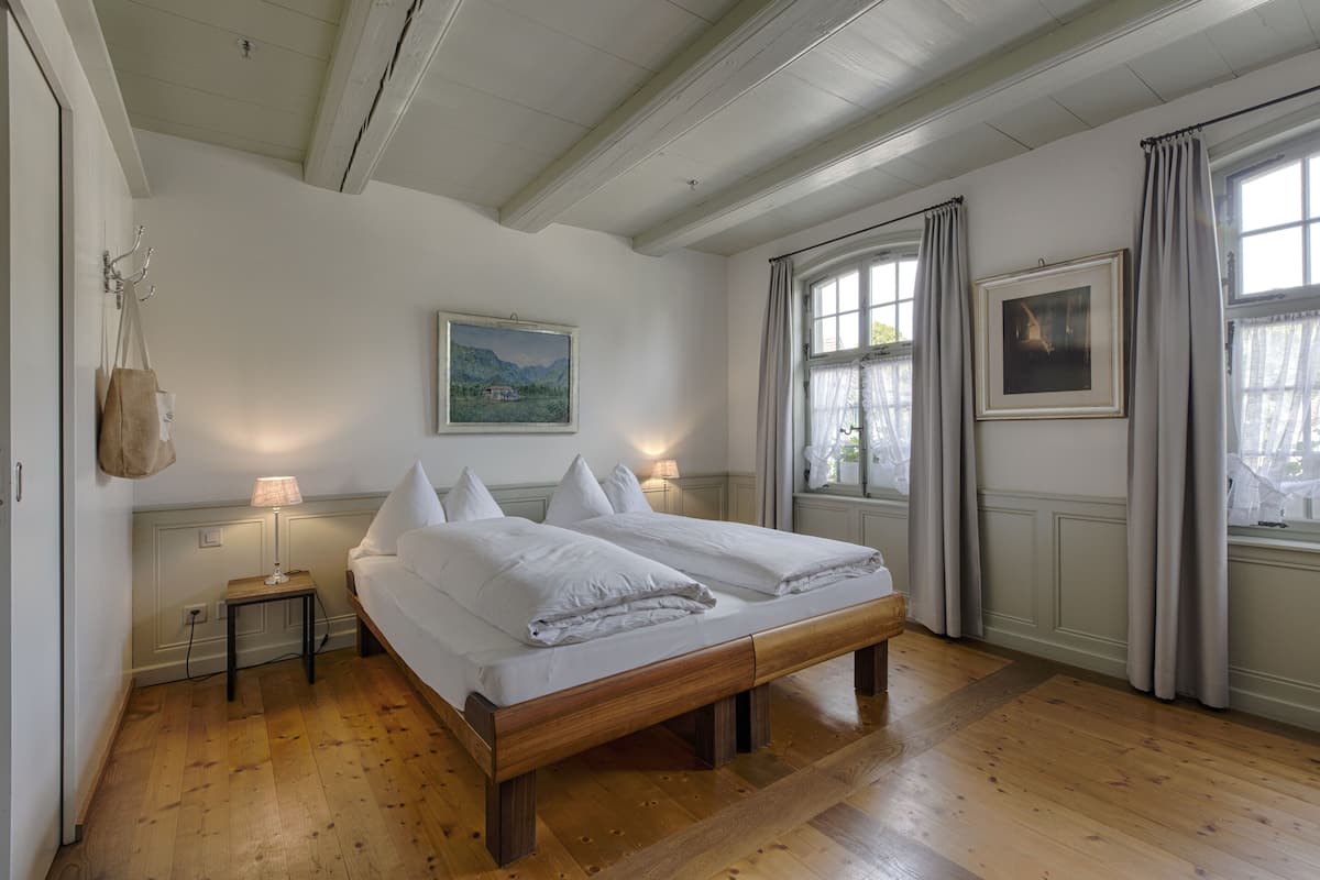 Un dormitorio con una cama de madera, dos mesitas de noche con lámparas, un cuadro en la pared y una ventana con cortinas.