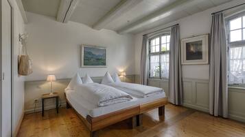 A bedroom with a wooden bed, two bedside tables with lamps, a painting on the wall, and a window with curtains.