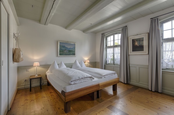 Un dormitorio con una cama de madera, dos mesitas de noche con lámparas, un cuadro en la pared y una ventana con cortinas.