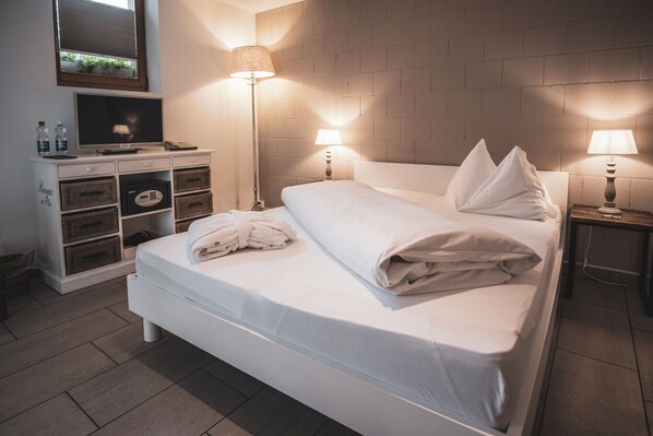 A neatly made bed with pillows, a bedside lamp, and a flat-screen TV on a dresser.