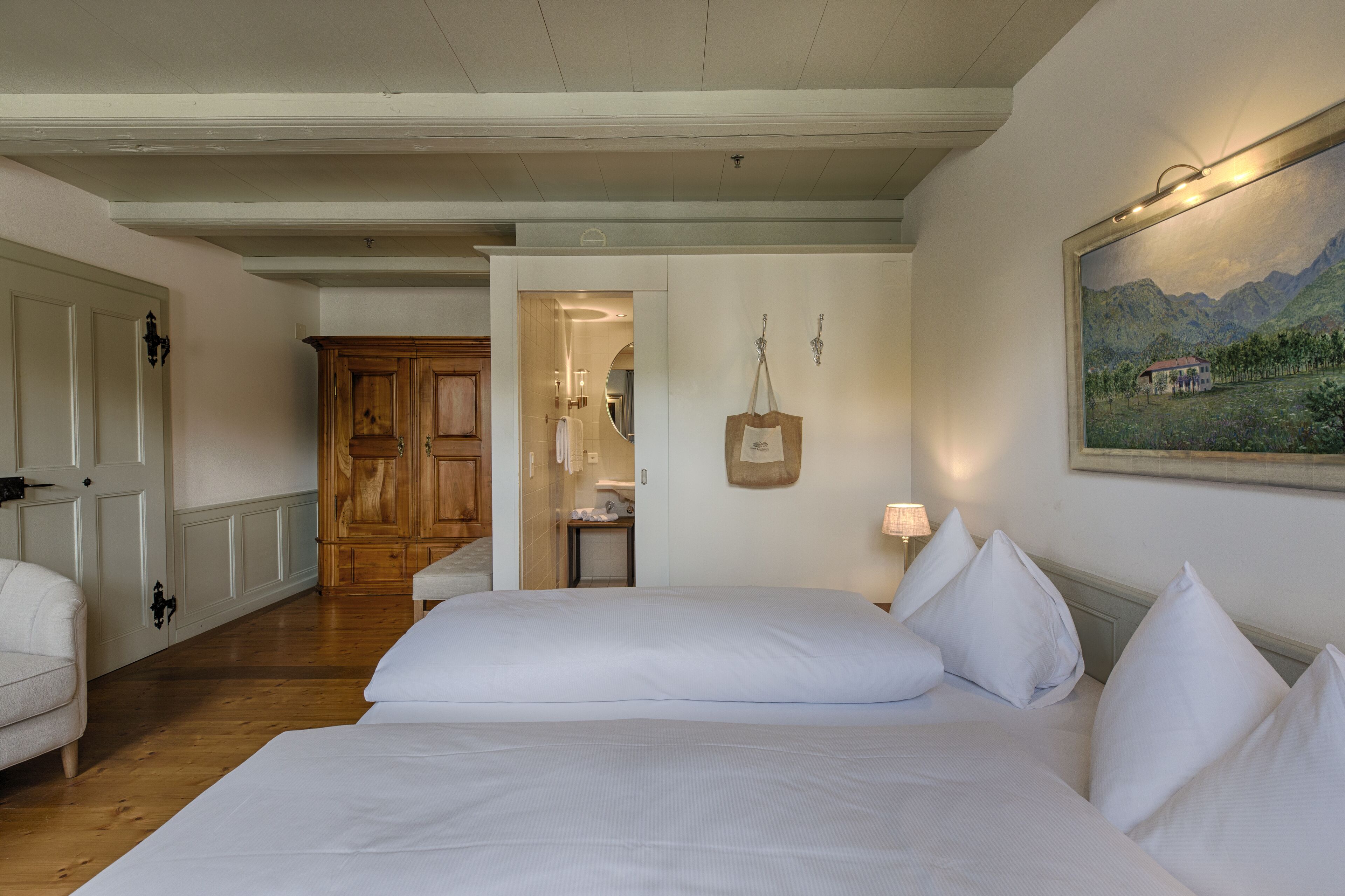 Habitación de hotel con una cama grande, un armario de madera, un baño con espejo y un cuadro en la pared.