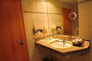 A hotel bathroom with a granite countertop sink, a large mirror, and a towel rack.