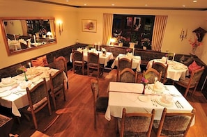 A dining area with multiple tables set for service, wooden chairs, and a large mirror on the wall.