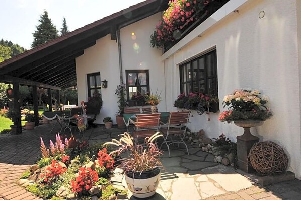 A white building with a covered patio area, outdoor seating, and potted plants.