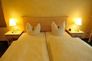 A double bed with two nightstands, each with a lamp, in a room with a plain wall and a wooden headboard.