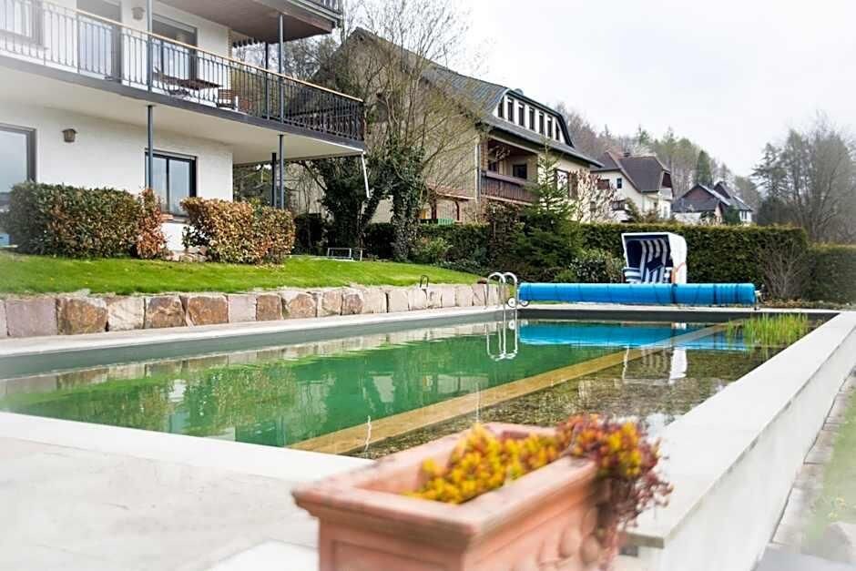 A residential area with a swimming pool, a two-story house with a balcony, and a hedge.