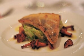 A plate with a piece of meat, possibly duck, accompanied by vegetables and sauce.