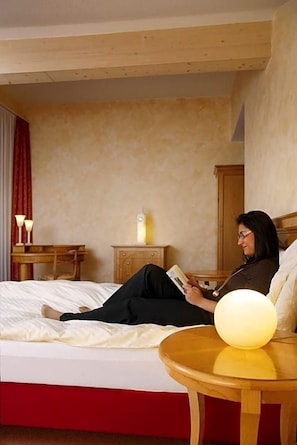 A hotel room with a bed, a bedside table with a lamp, a nightstand, and a wooden headboard.