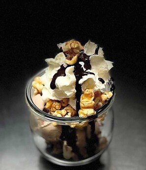 A dessert in a glass jar with whipped cream, chocolate drizzle, and nuts.