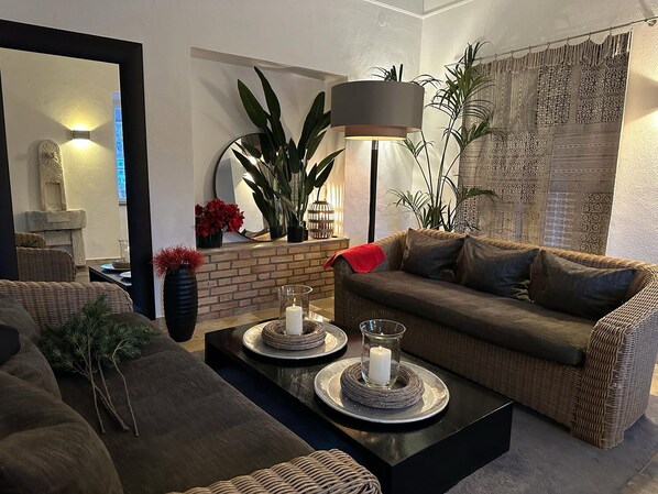 A cozy living room with a brown sofa, a black coffee table, and a large floor lamp. There are potted plants and a fireplace in the background. - Hotel Schloss Ort (Passau)