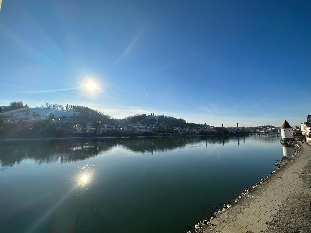 Ein ruhiger Fluss unter einem klaren Himmel, in der Ferne eine Stadt.
