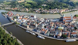 An aerial view of a riverside town with historic buildings, a bridge, and boats docked along the river. - Hotel Schloss Ort (Passau)
