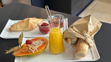 Un plato de desayuno con un croissant, media papaya con semillas, un vaso de zumo de naranja y un sándwich envuelto en papel.