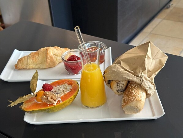A breakfast plate with a croissant, a half-cut papaya with seeds, a glass of orange juice, and a sandwich wrapped in paper. - Hotel Schloss Ort (Passau)